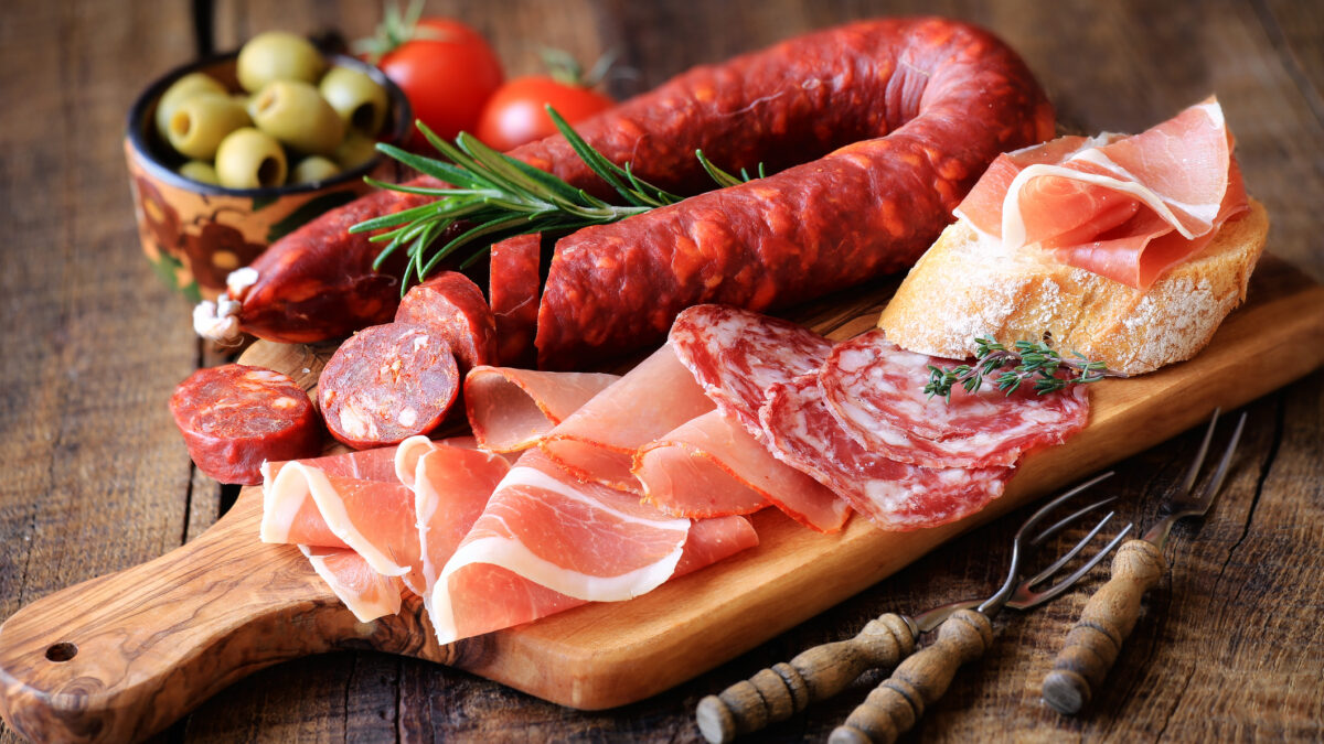 Cured meat platter of traditional Spanish tapas - chorizo, salsichon, jamon serrano, lomo - erved on wooden board with olives and bread